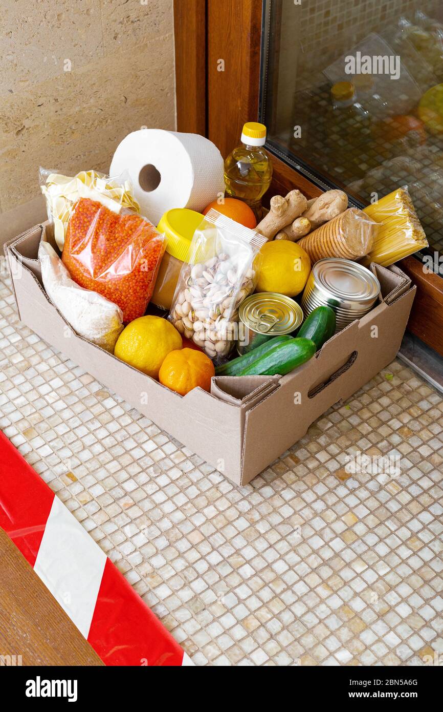 Box mit Lebensmitteln während der Selbstisolation covid Quarantäne zu Hause. Die Lieferung der Foodbox vor der Tür hinter der Schlange. Kontaktlose Lieferung, sicher Stockfoto
