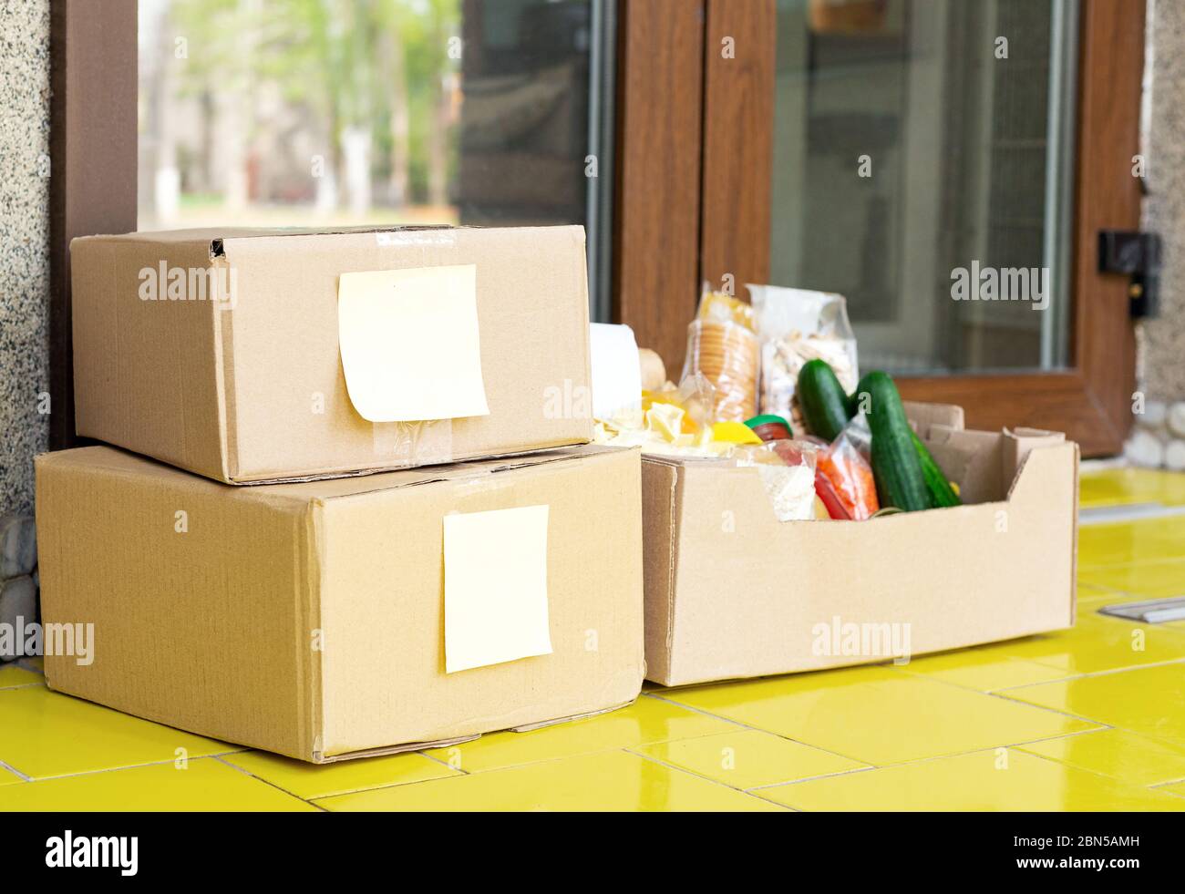 Lieferung von Lebensmitteln. Boxen mit lebenswichtigen Gütern, Sozialhilfe, langfristige Lagerprodukte vor der Haustür in der Nähe der Haustür. Kontaktlose Lieferung von sozialen Netzwerken Stockfoto