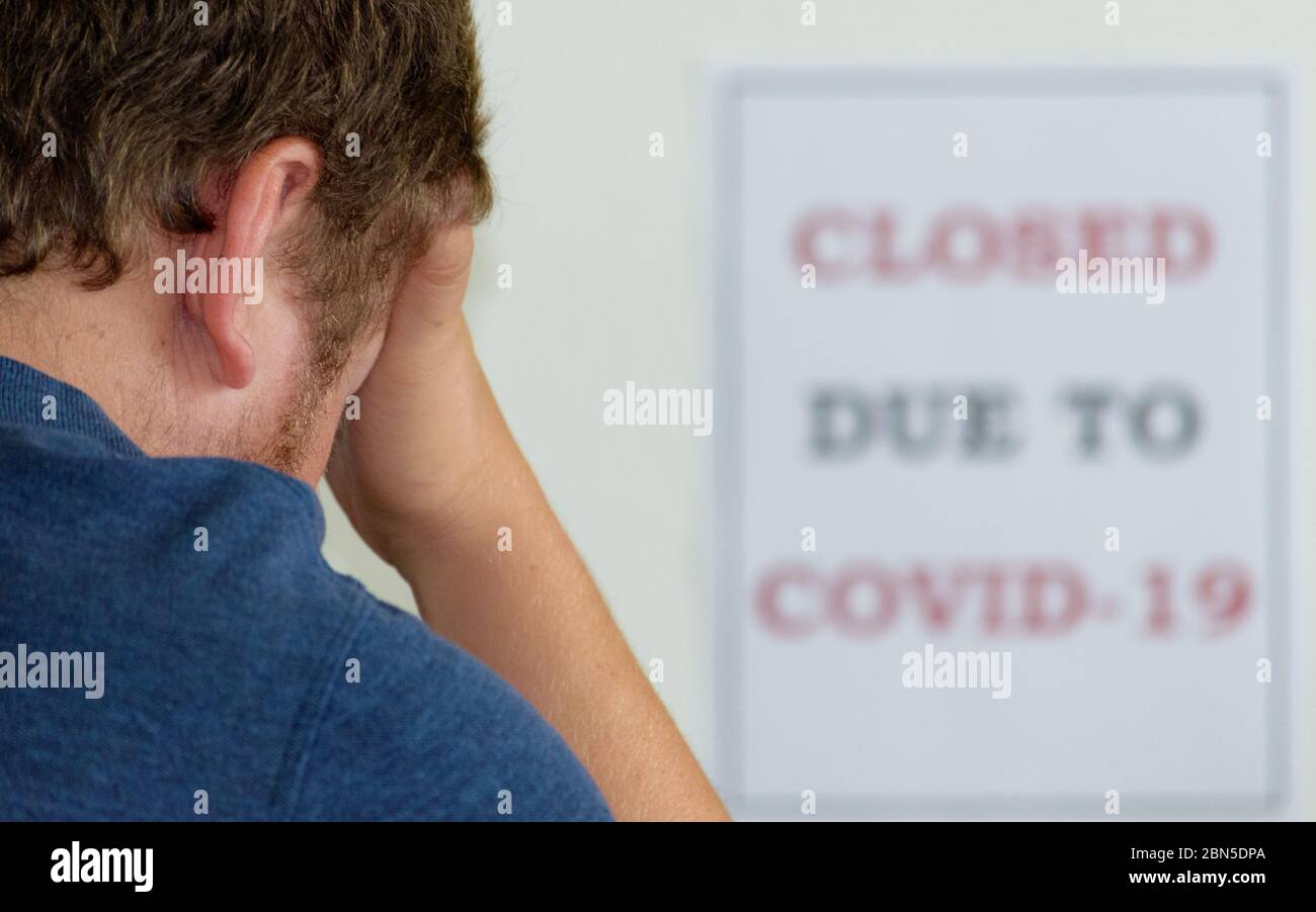 Junger Mann mit dem Kopf in den Händen in Verzweiflung während der Covid-19 / Coronavirus Pandemie Stockfoto