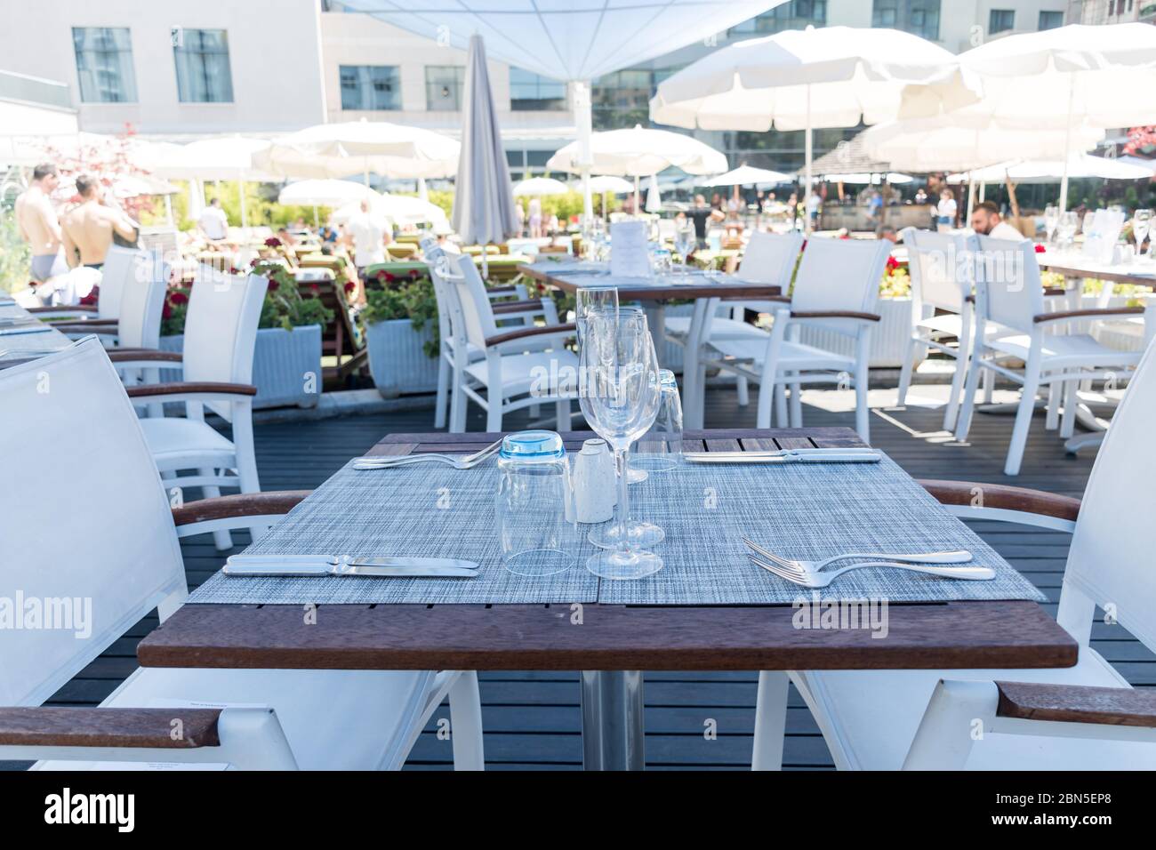 Terrasse mit Tisch. Niemand auf dem Bild nur Tischaufstellung mit Besteck und Gläsern. Pool mit Sonnenliegen im Hintergrund. Blau und Holz ta Stockfoto