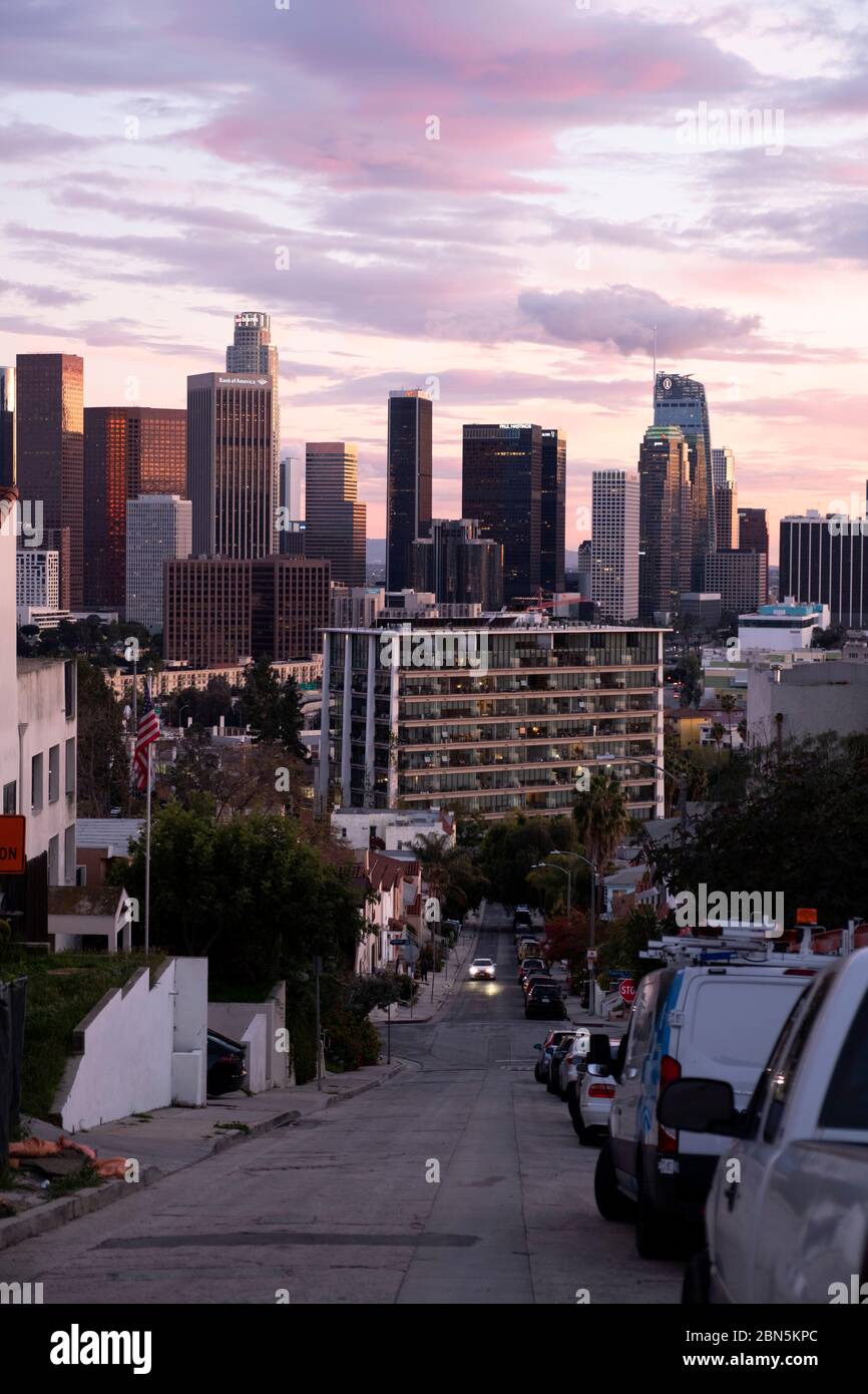 Blick auf eine hügelige Wohnstraße in Los Angeles bei Sonnenuntergang mit Blick auf die Innenstadt VON LA Stockfoto