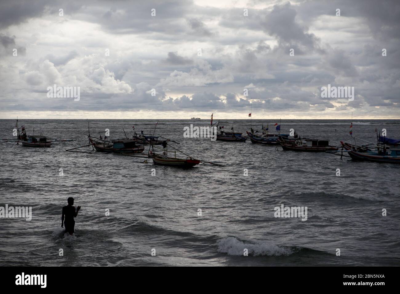 Ein Fischerdorf an der Westküste Sumatras im Dezember Ein Fischer, der im seichten Wasser steht und auf die ankernden Fischerboote am Küstenwasser des Malabro-Strandes in Bengkulu blickt, einer Stadt an der Westküste Sumatras mit Blick auf den Indischen Ozean. Archivbild. 1.. Dezember 2012. Stockfoto