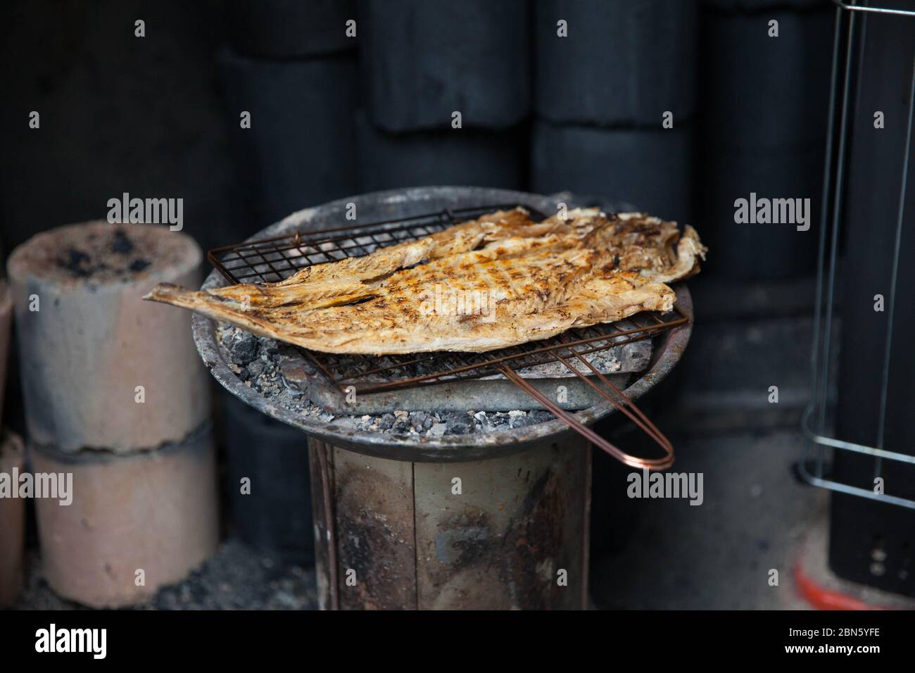 Fisch wird auf einem Holzkohlefire auf einem kleinen Drahtschrank gegrillt. Koreanischer traditioneller getrockneter Fisch auf einem Grill. Stockfoto