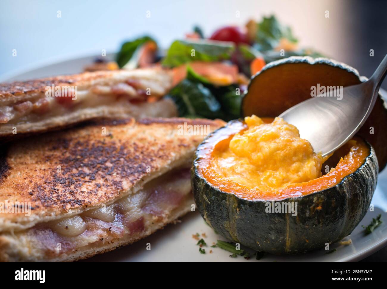 Ein Löffel Kürbissuppe in einer Mini-Kürbisschale. Toast Brot zum Brunch mit Gemüse. Stockfoto
