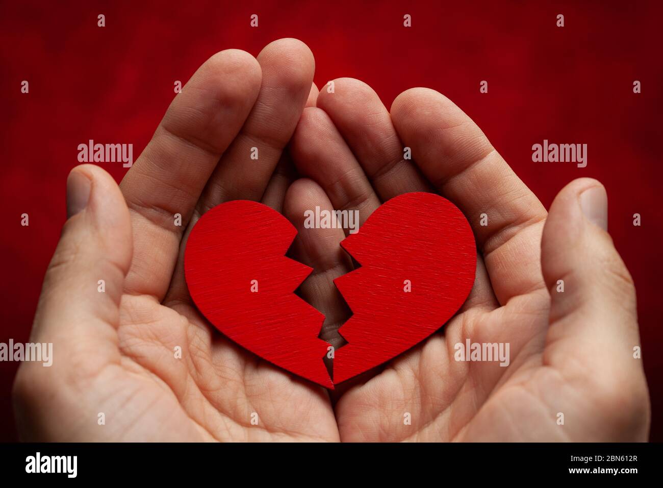 Der Mensch hält ein gebrochenes Herz in seinen Händen. Riss in das rote Herz, die Beziehung zu brechen. Stockfoto