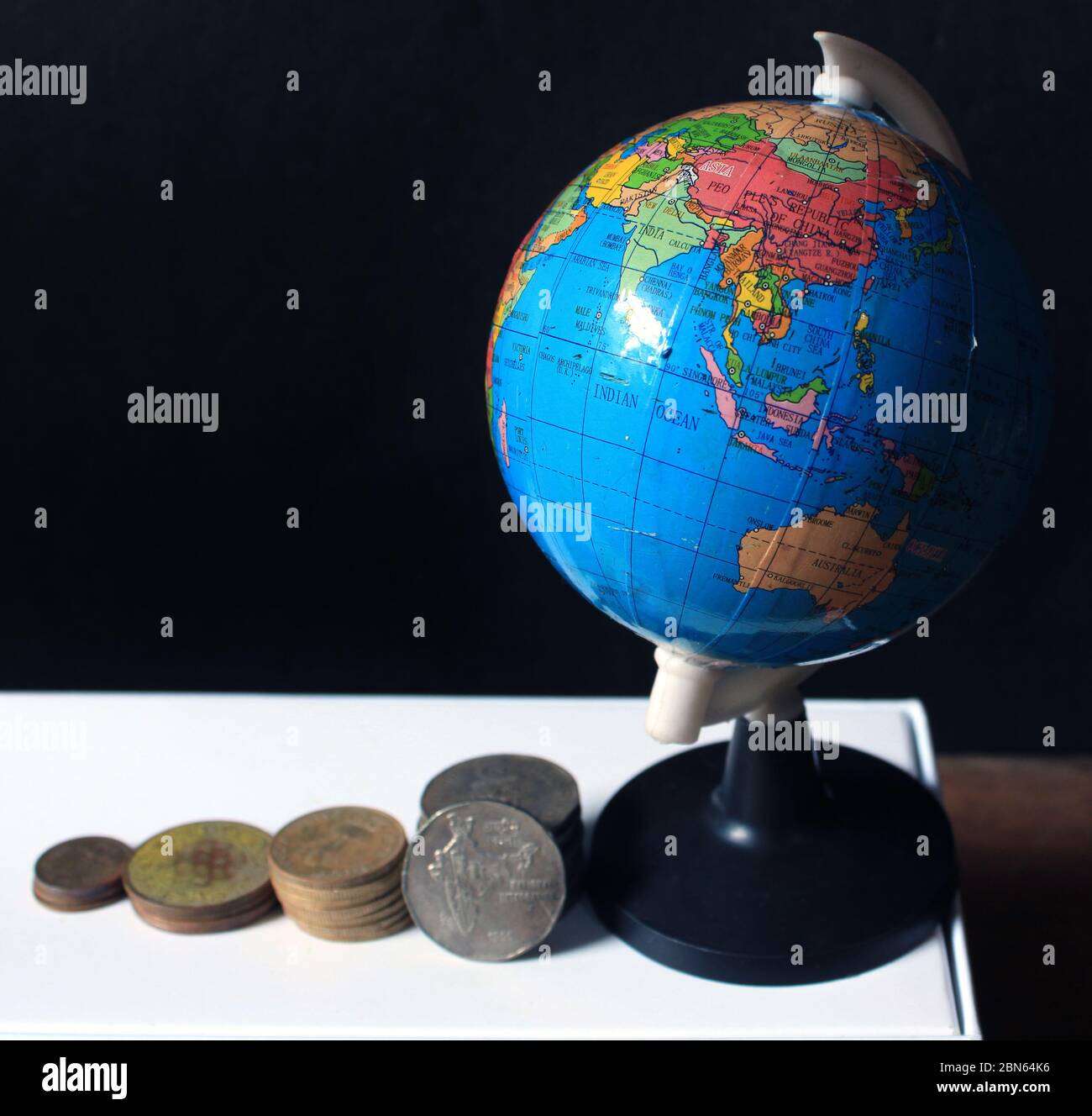 Stapel von indischen Münzen über schwarzem Hintergrund mit Globus-Karte. Geschäftsmetapher, Finanzinvestition und Wirtschaftskonzept. Stapel von indischen Münzen in Bar Stockfoto