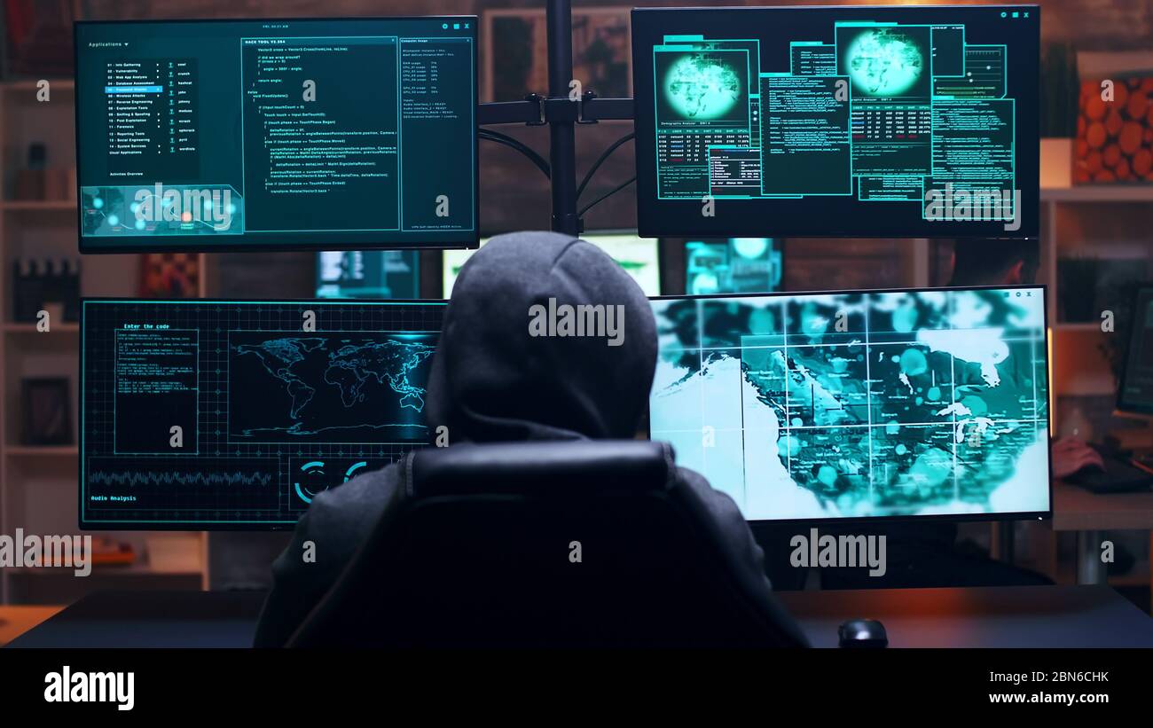 Rückansicht des männlichen Hackers, der einen Hoody trägt, der einen Regierungsserver mit einem gefährlichen Virus infiziert. Stockfoto