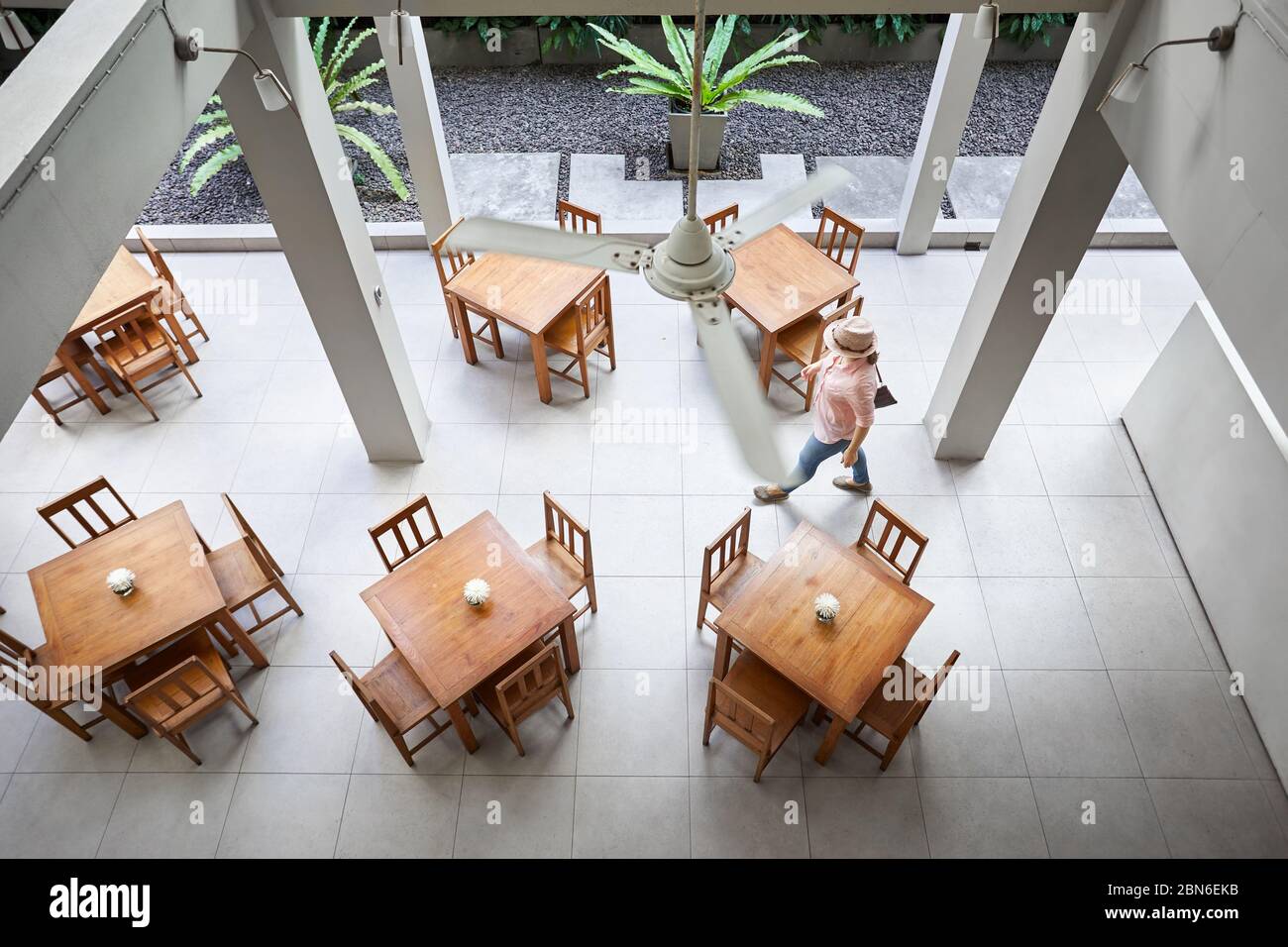 Frau in rosa Hemd und Hut ist zu Fuß in der Nähe des Tisches im Hotel Restaurant in Bangkok. Ansicht von oben. Stockfoto