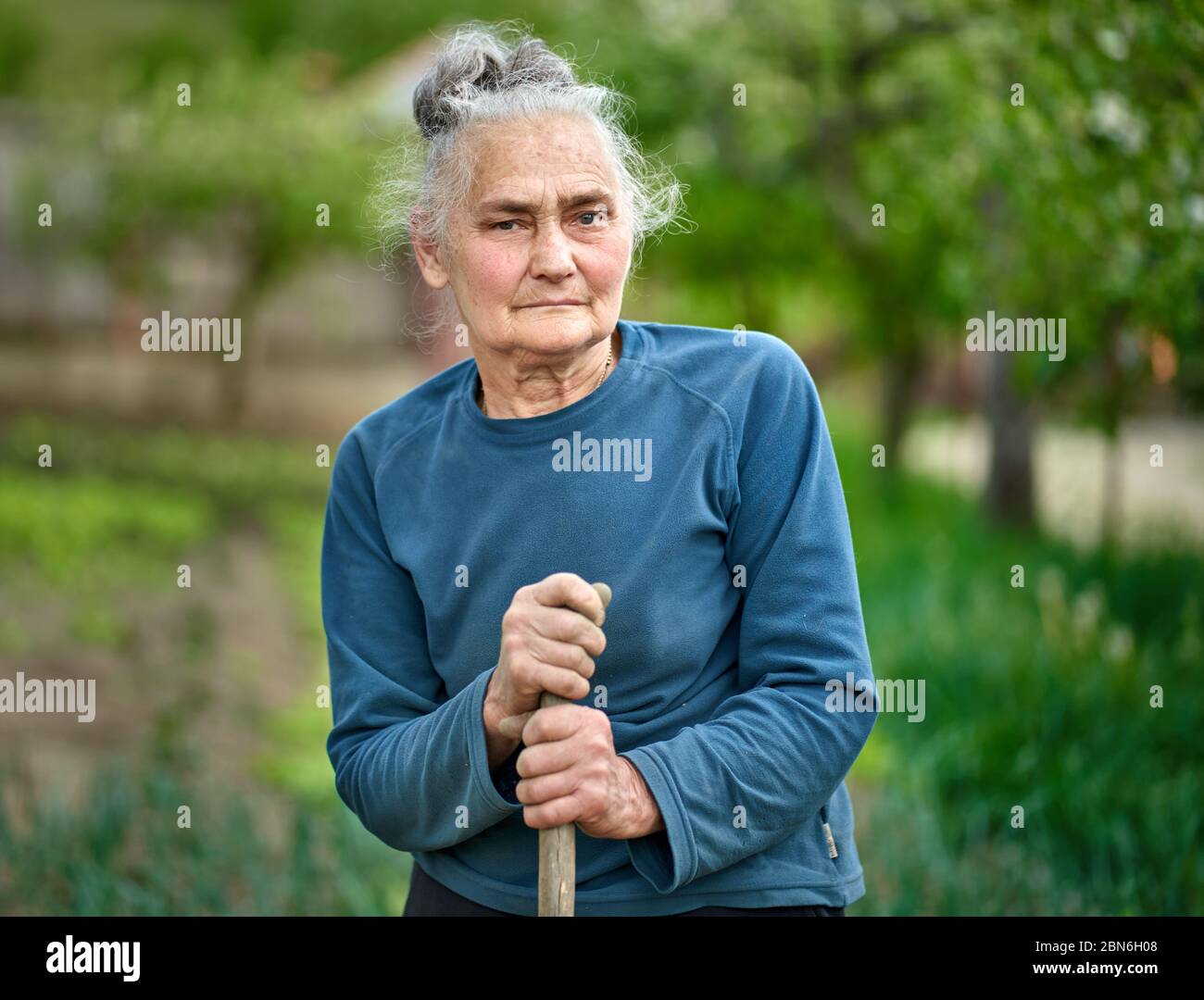 Alte Bäuerin mit Hacke in ihrem Garten Stockfoto