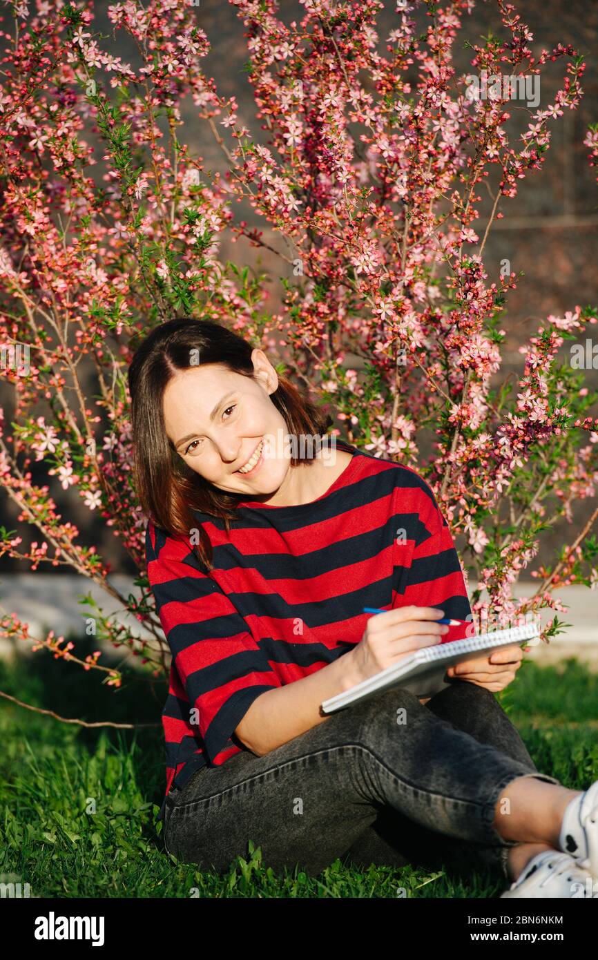Lächelndes Mädchen im Garten mit einem Notizbuch und Stift in den Händen Stockfoto