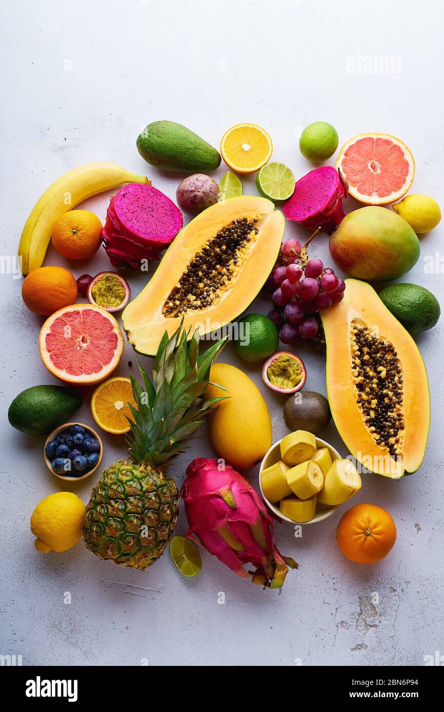 Tropisches Fruchtmuster mit Mango, Papaya, Pitahaya, Passionsfrucht, Trauben, Limetten und Ananas. Tisch mit Zutaten für Sommernaschen auf Beton Stockfoto