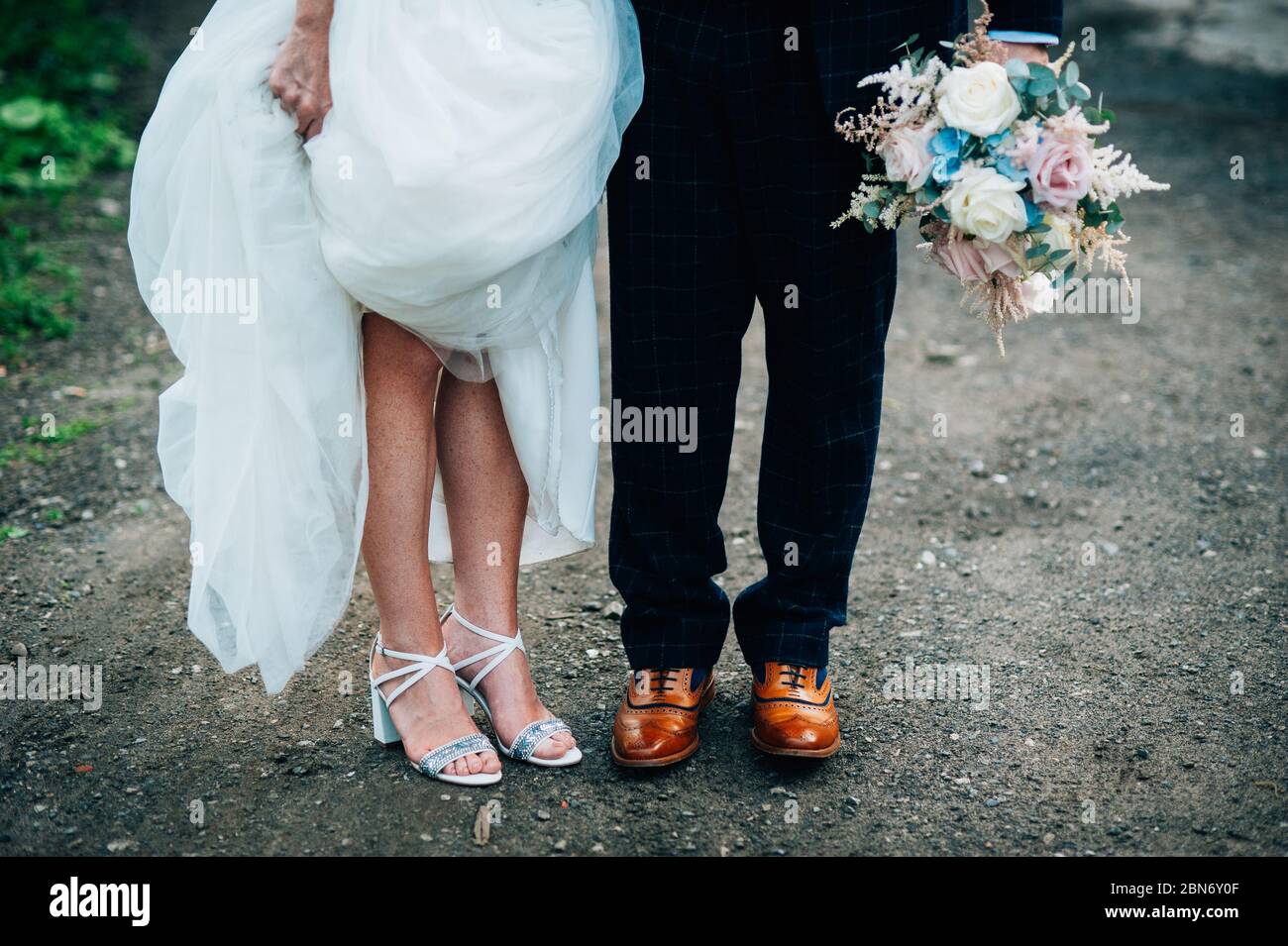 Englische Hochzeitsfotografie, Braut und Bräutigam stehen zusammen und zeigen ihre Schuhe. Schrullig Stockfoto