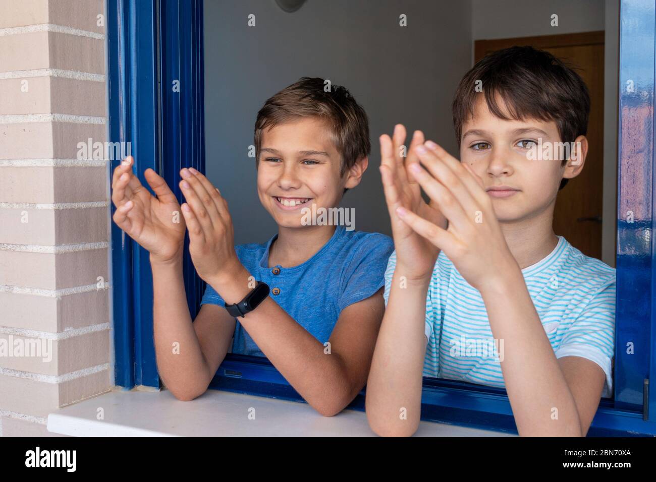 Glücklich lächelnde Kinder klatschen Hände, applaudieren vom Fenster, um Ärzte, Krankenschwestern, Krankenhausangestellte während Coronavirus Covid-19 Pandemie Quarantäne zu unterstützen Stockfoto