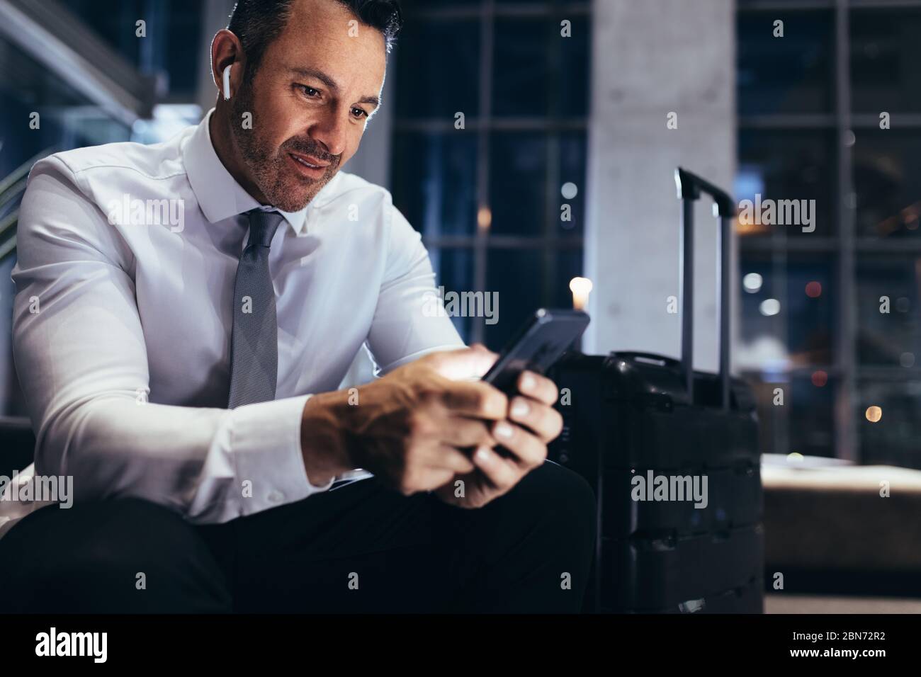 Geschäftsmann wartet am Flughafen erstklassige Lounge mit Gepäck neben ihm. Mann in formalwear sitzt am Flughafen Abflugbereich mit seinem intelligenten ph Stockfoto