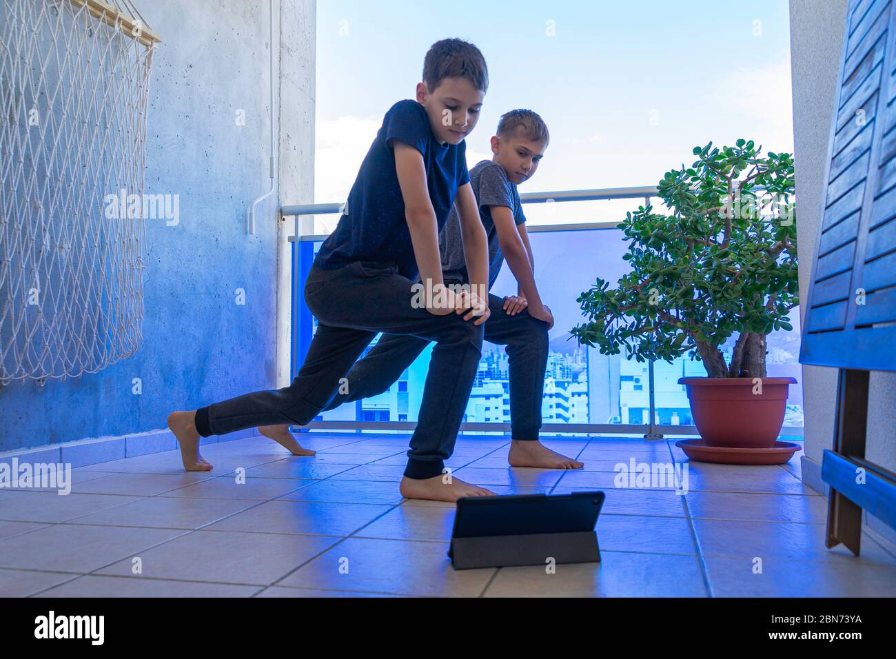 Jungs mit Tablet-Computer, die Sport-Übungen auf dem Balkon. Sport, gesunder Lebensstil, aktive Freizeit zu Hause Stockfoto