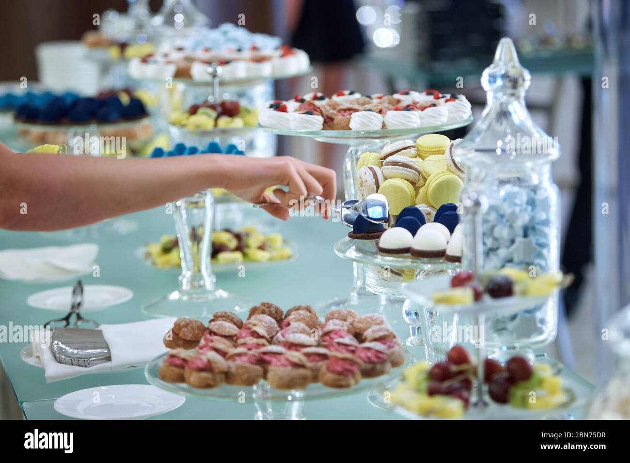 Weibliche Hände nehmen Kuchen mit einer Zange von einem Banketttisch mit Süßigkeiten gelegt Stockfoto