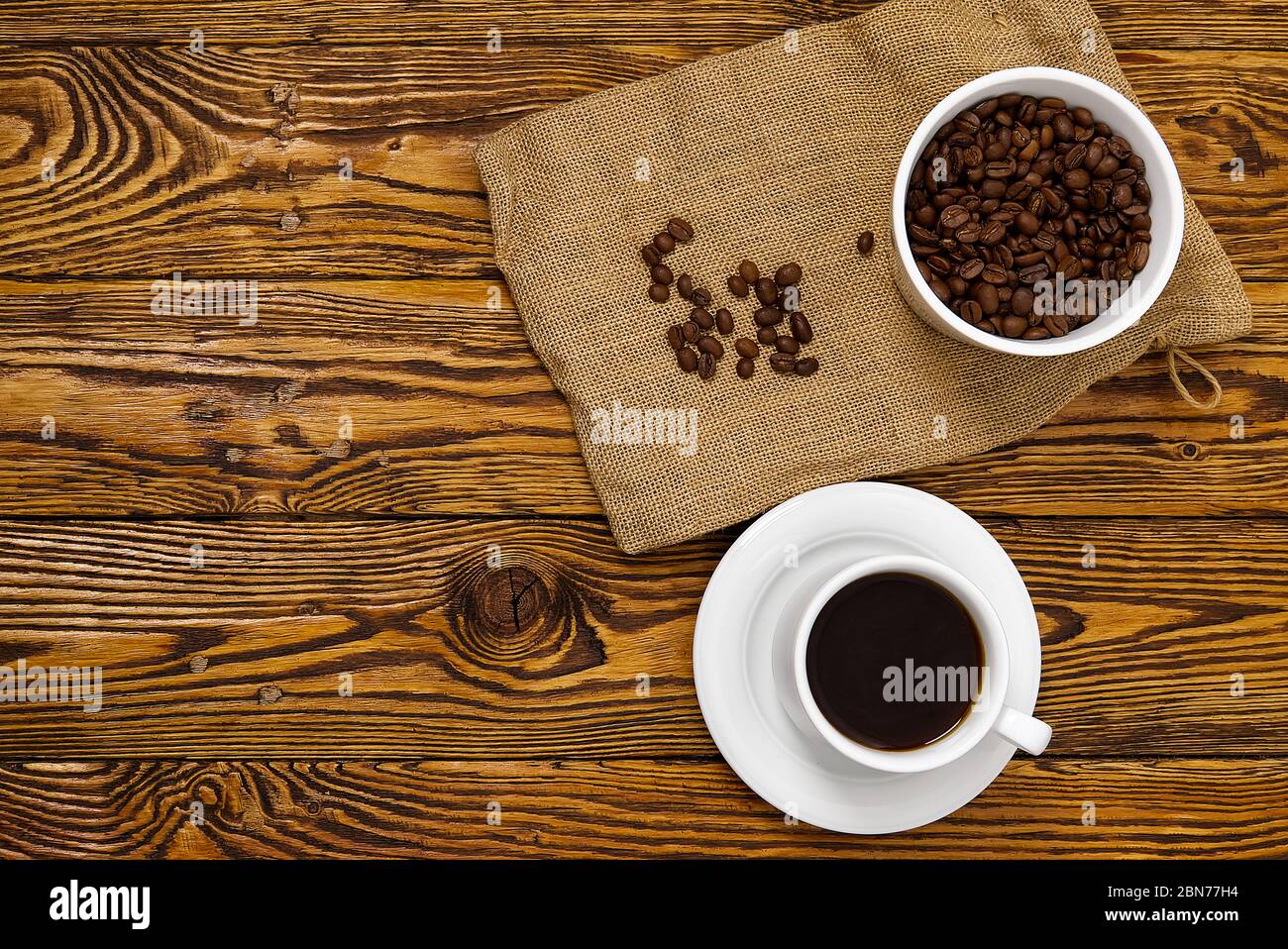 Weiße Kaffeetasse mit aromatischem Kaffeegetränk auf braunem Holztisch. Kaffeesamen auf antikem Holztisch mit Tasse Kaffee Getränk Stockfoto