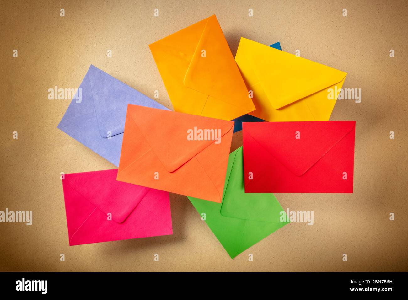 C6-Umschläge fliegen über einem braunen Kraftpapier Hintergrund, in verschiedenen Farben Stockfoto