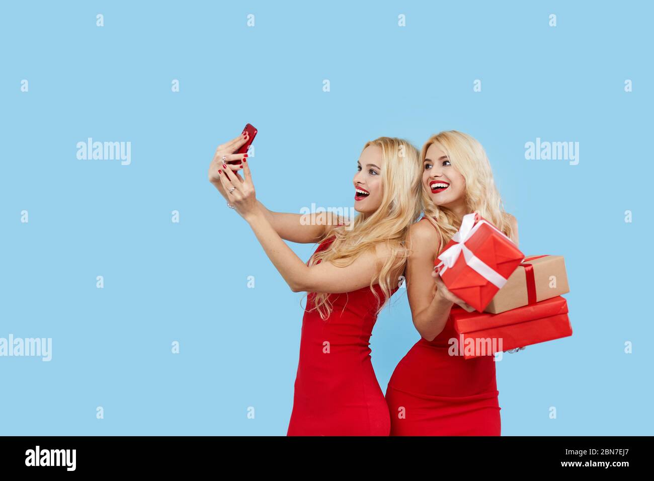 Urlaubsangebote. Happy Women mit Geschenkboxen in roten Kleidern auf blauem Hintergrund, macht Selfie auf Smartphone. Weihnachtsgeschenke.Einkaufszentrum Stockfoto