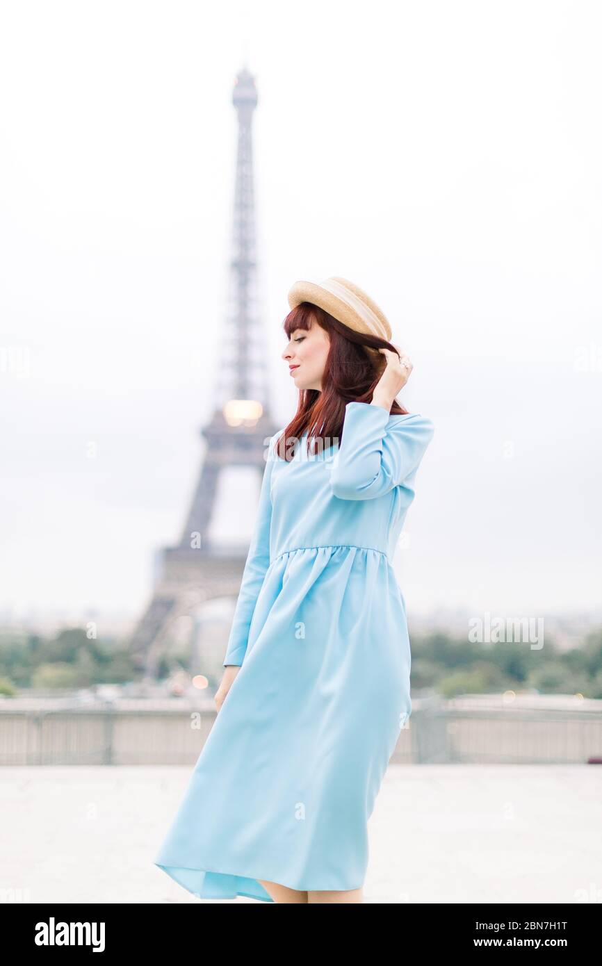 Schönes Mädchen mit langem blauen Kleid und Strohhut, posiert und genießen den Moment in Paris mit Eiffelturm auf Hintergrund. Stockfoto
