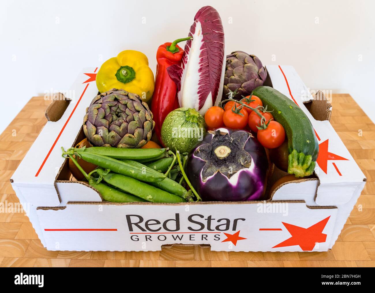 Gemüsebox mit Paprika, Endive, Aubergine, Artischocken, Erbsenschoten und Kirschtomaten Stockfoto
