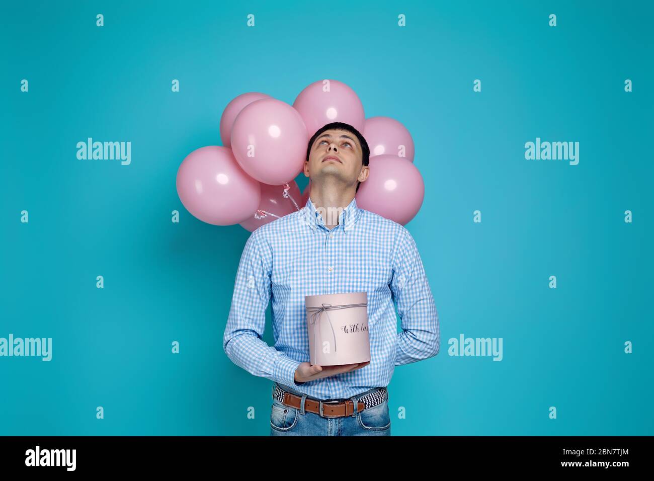 Glücklich kaukasischen Mann hält Geschenkbox und pastellrosa Luftballons auf blauem Hintergrund isoliert. Geburtstagsfeier. Stockfoto