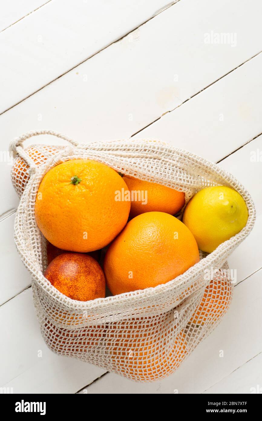 Orange, Zitrone und Grapefruit in Öko-Tasche auf weißem Holzhintergrund. Zitrusfrüchte. Zero Waste, umweltfreundliches oder plastikfreies Lifestyle-Konzept. Kopierbereich, vertikal. Stockfoto