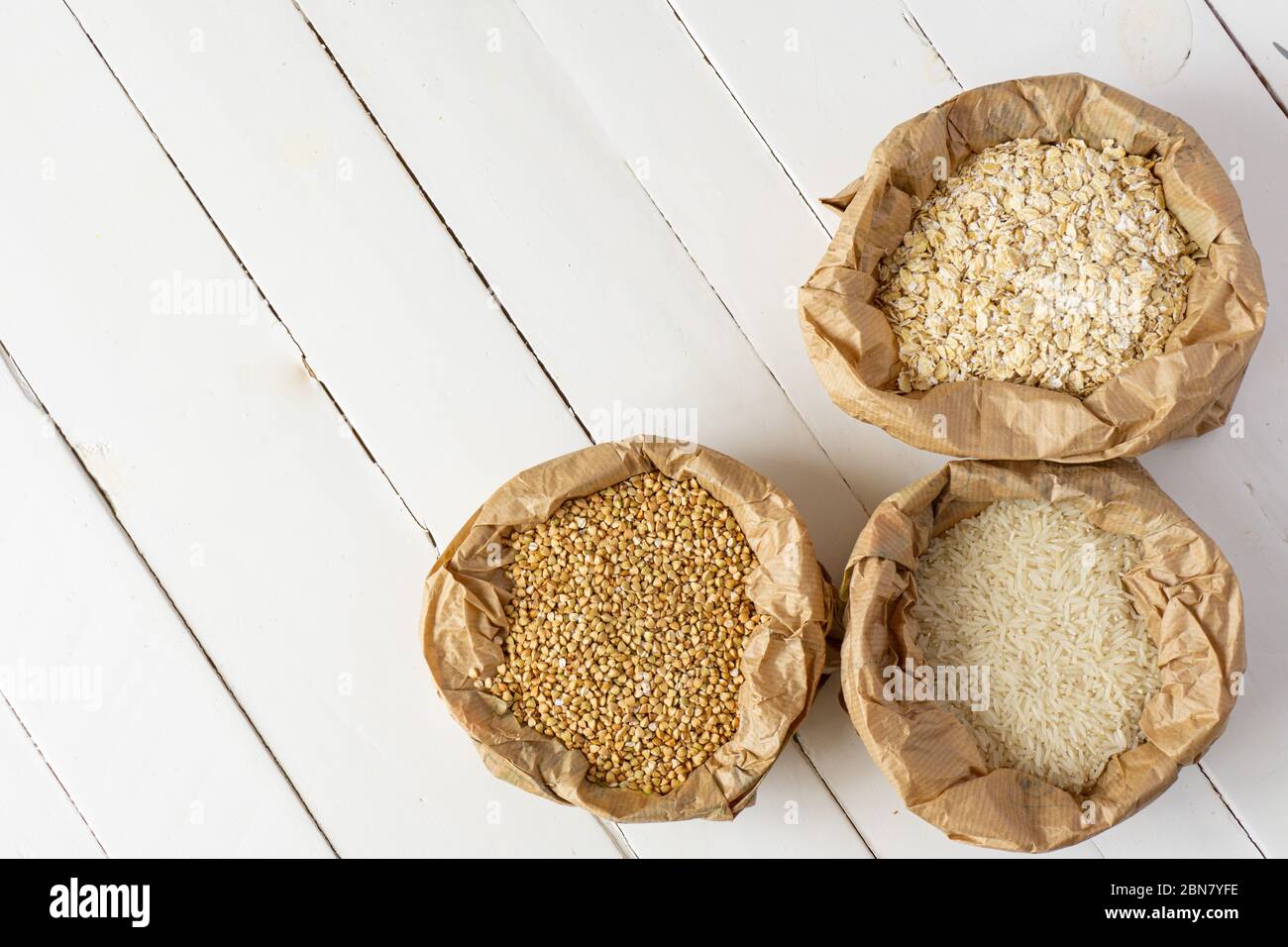 Hafer, Buchweizen, Reis in Papiertüten auf weißem Holztisch. Draufsicht, Kopierbereich. Zero Waste, umweltfreundliches oder plastikfreies Lifestyle-Konzept. Stockfoto