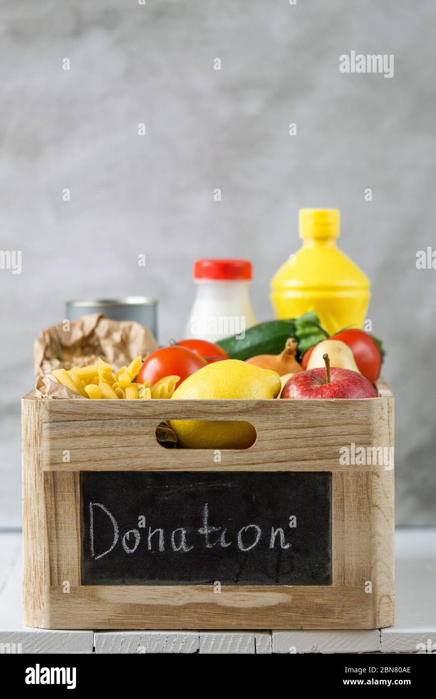 Lebensmittelspende Holzkiste mit Gemüse, Obst, Pasta, Öl, Milch und Konserven. Kopierbereich, vertikal Stockfoto