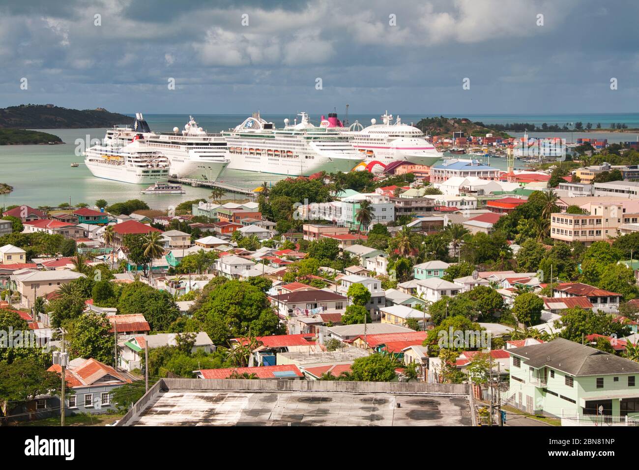 Vier Kreuzfahrtschiffe, die im Hafen von St. Johns, Antigua in der Karibik, Westindien, festgemacht sind, scheinen die Stadt durch ihre Größe zu dominieren Stockfoto