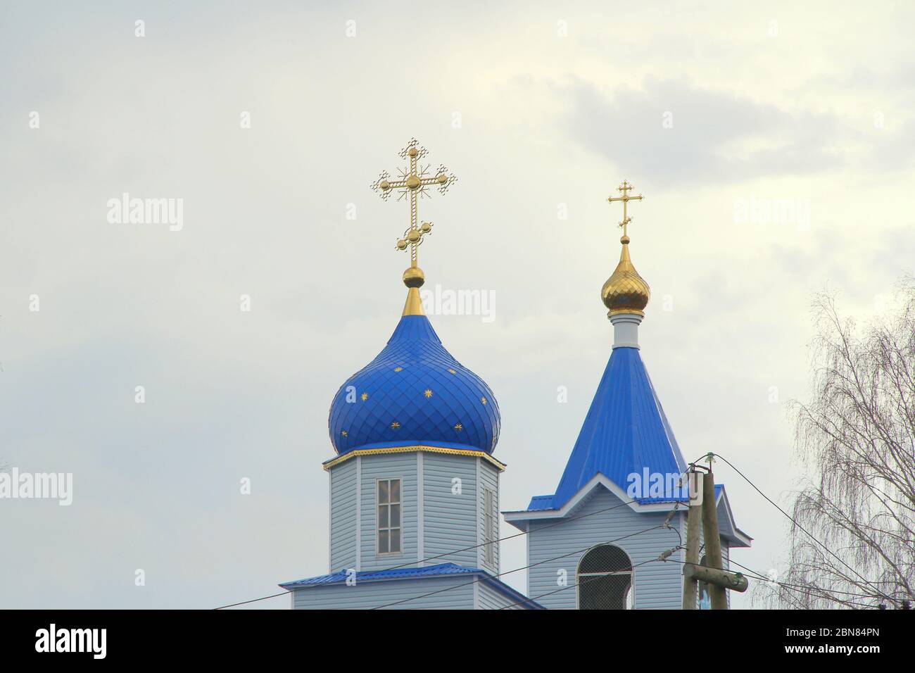 Orthodoxe christliche Kirche mit weißen Wänden, blauen Kuppeln und goldenen Kreuzen in Russland. Ein Gebäude für religiöse Zeremonien mit einem Glockenturm vor einem bewölkten Himmel auf dem Land. Stockfoto
