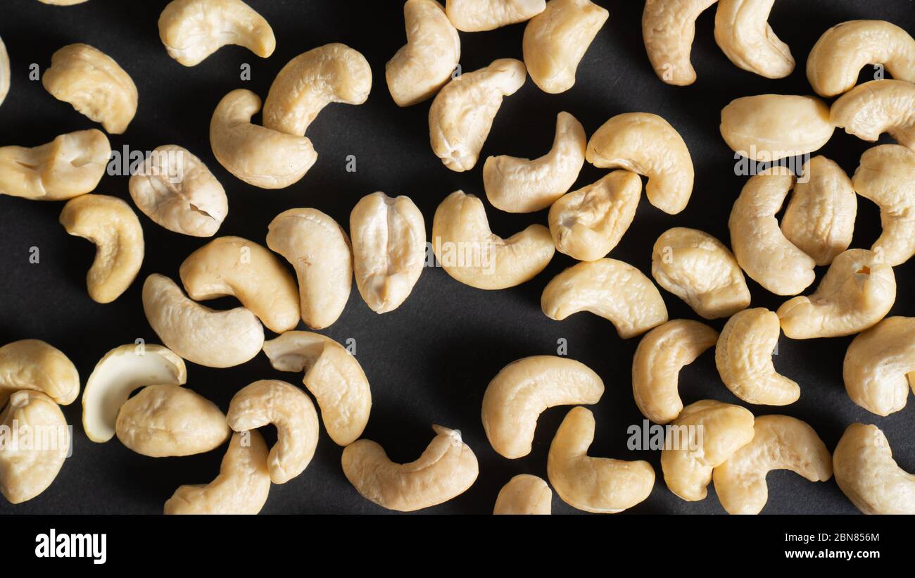 Draufsicht auf verstreuten Cashewnüssen auf schwarzem Hintergrund. Nüsse für die Gesundheit des Herzens, Augen und gut für die Haut. Gesunde Nüsse. Stockfoto