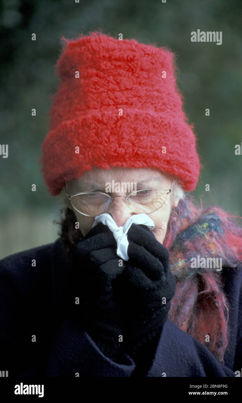 Ältere Frau in Winterkleidung weht Nase Stockfoto