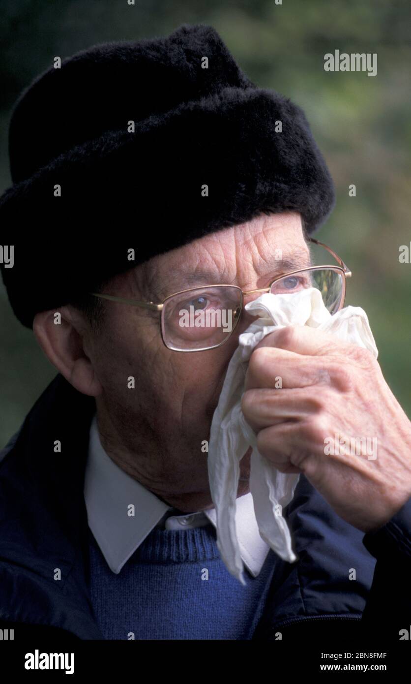 Älterer Mann in Winterkleidung weht Nase Stockfoto