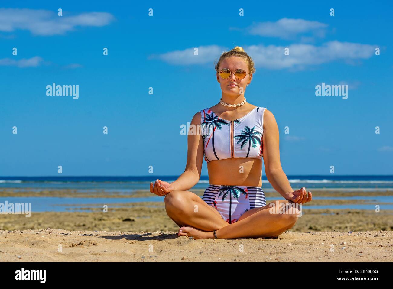 Junge kaukasische Frau im Bikini meditiert am Strand mit Meer Stockfoto
