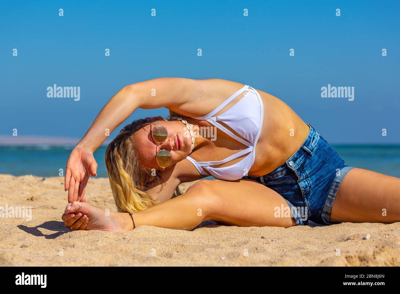 Blonde junge kaukasische Frau Biegen Seitenwand im Sand am Strand Stockfoto