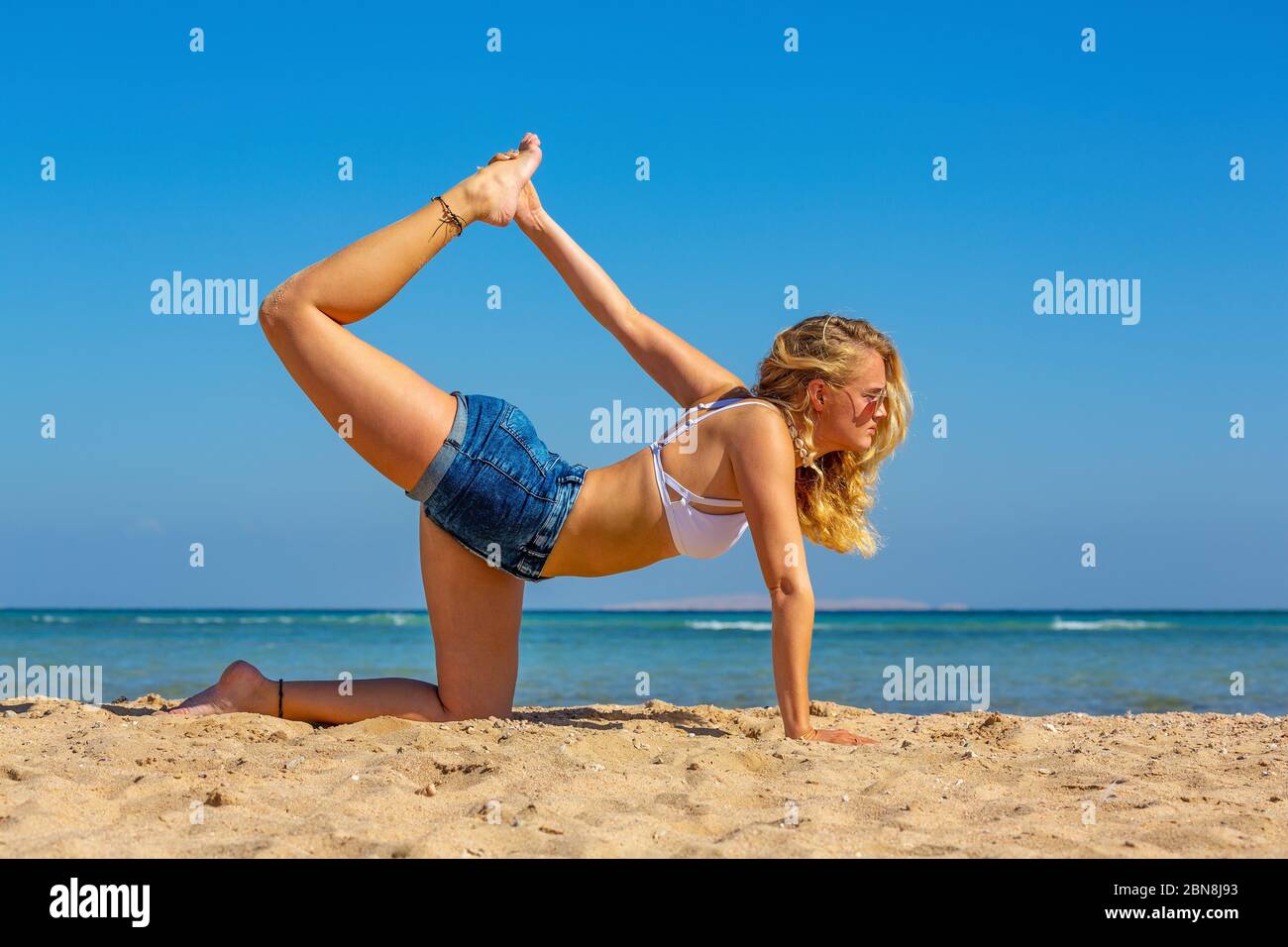 Junge kaukasische Frau in Yoga-Haltung am ägyptischen Strand Stockfoto