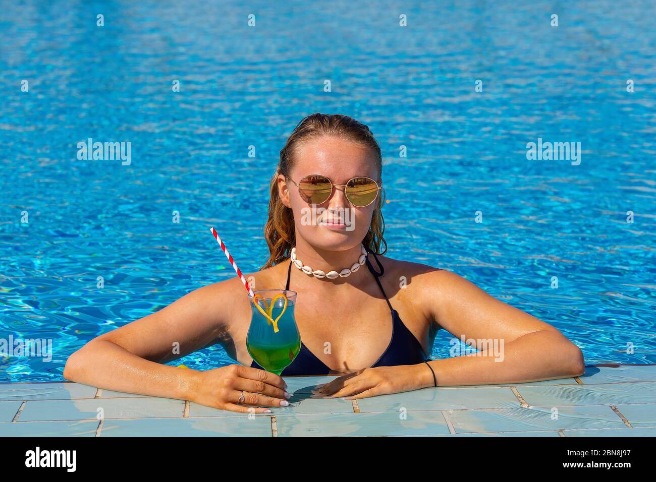 Junge europäerin hält Cocktail-Drink im blauen Schwimmbad Stockfoto