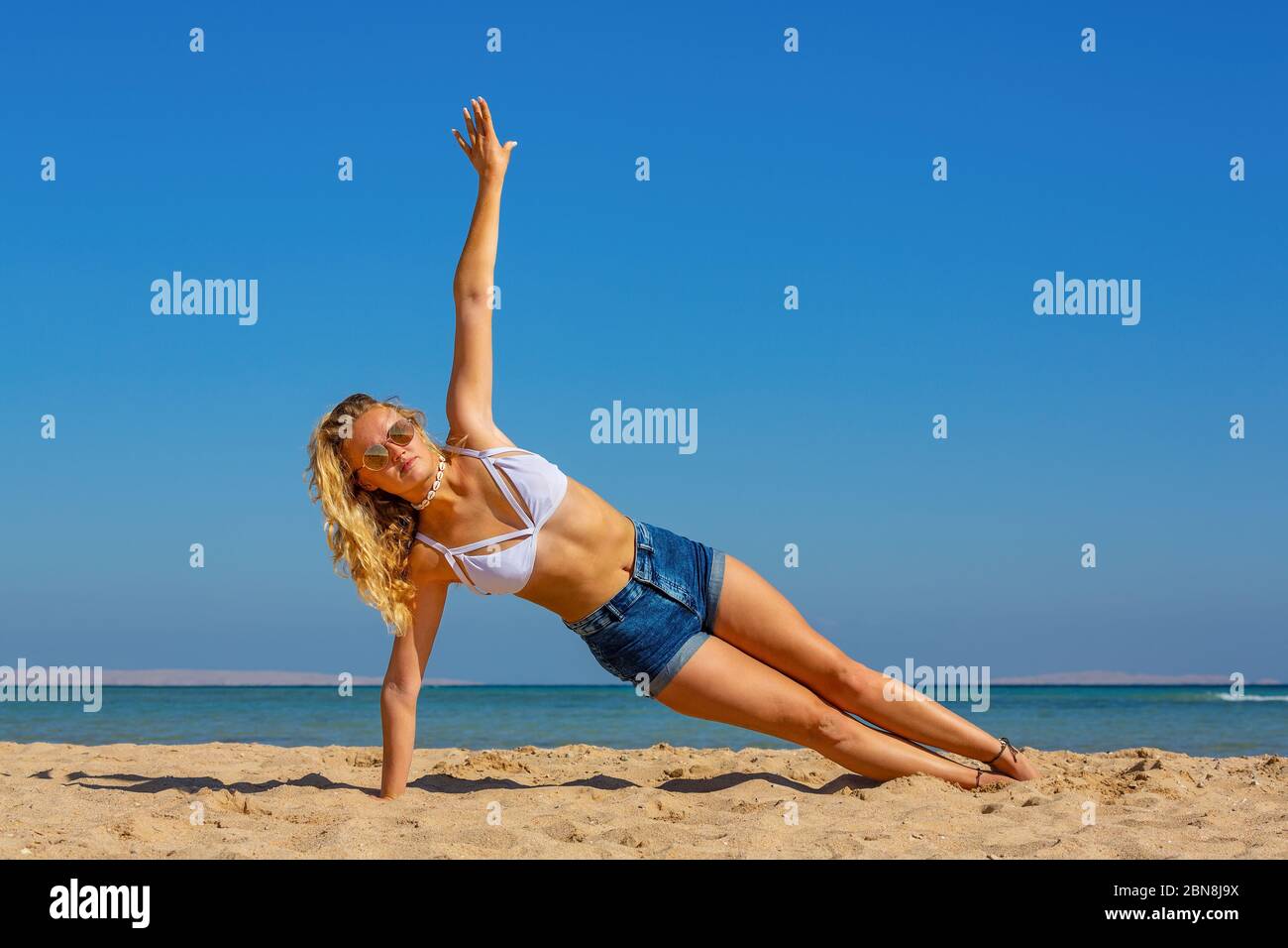 Junge holländerin planking seitlich am Strand mit blauem Himmel Stockfoto