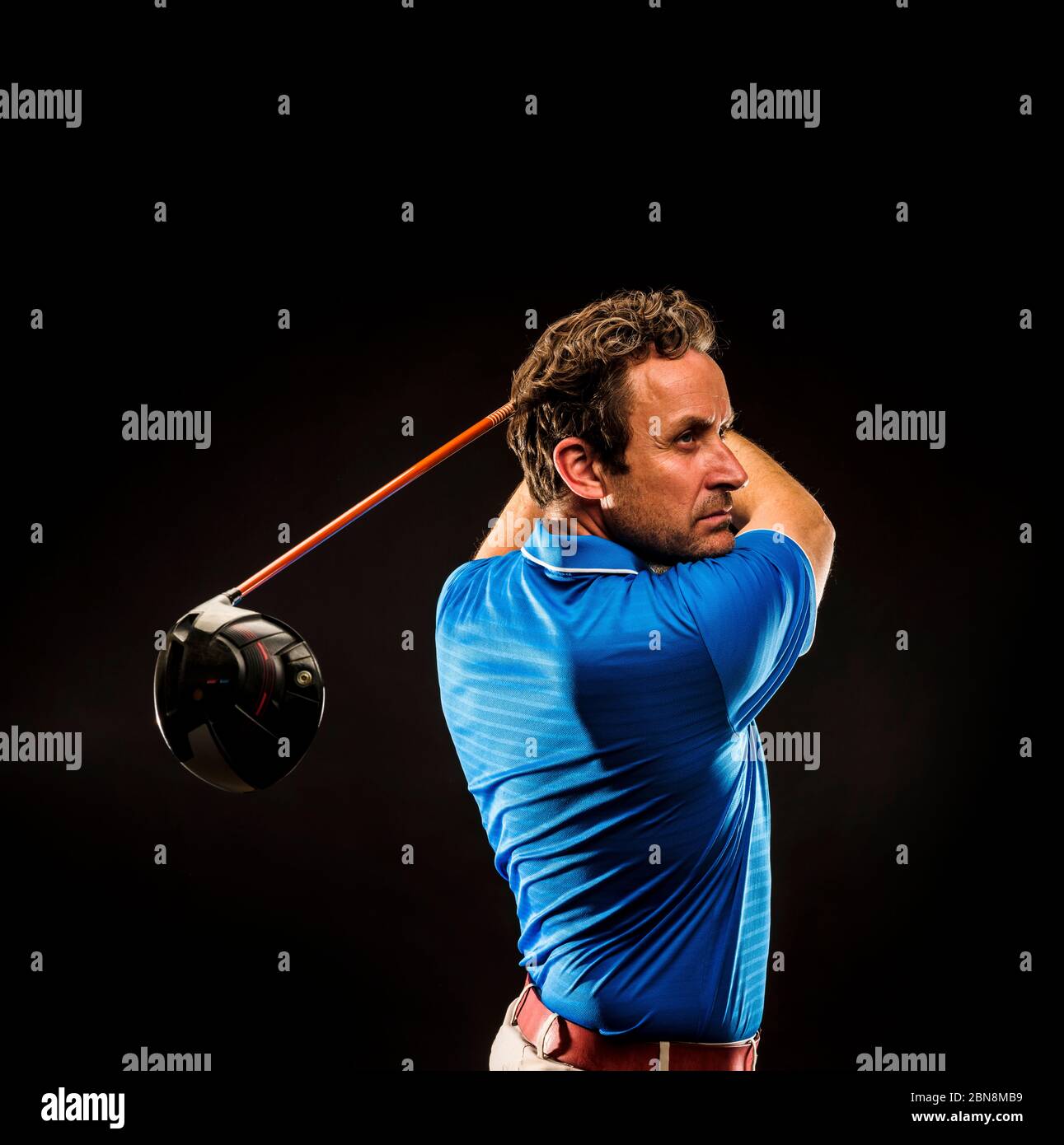 Porträt eines Golfspielers, der den Schwung isoliert auf dunklem Hintergrund perfektioniert Stockfoto