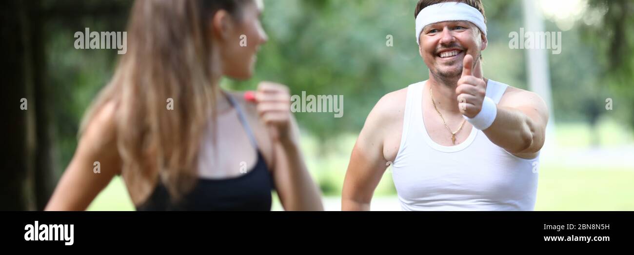 Der Mann im Park zeigt dem Sportmädchen eine Geste. Stockfoto