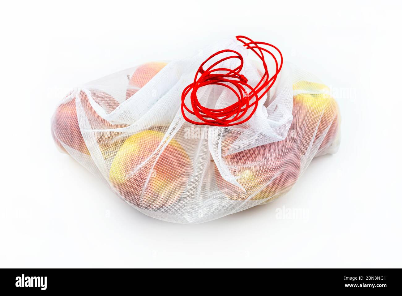 Reife Äpfel verpackt in einem weißen wiederverwendbaren Netzbeutel mit roter Schnur, isoliert auf weißem Hintergrund. Stockfoto