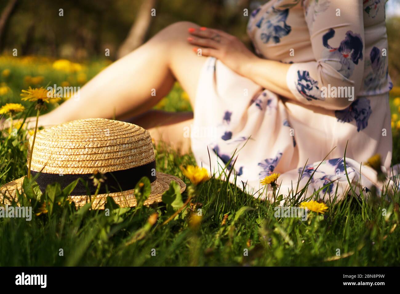Frau mit einem Strohhut in einem Blumenfeld und grünem Gras. Sommer auf dem Land. Konzentrieren Sie sich auf Hut Stockfoto