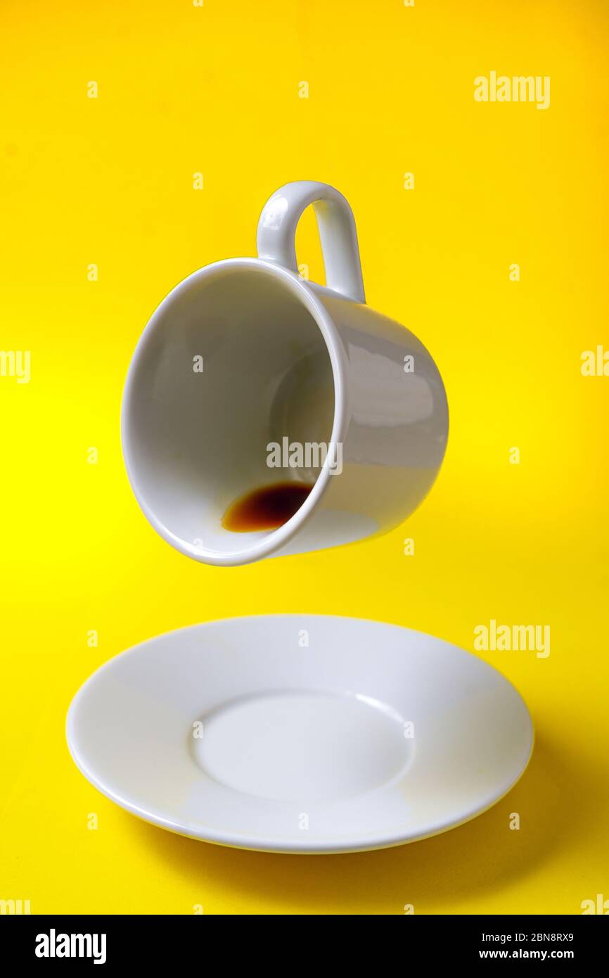 Weiße Tasse Kaffee mit Kaffee schweben in der Luft und eine Untertasse auf einem gelben Hintergrund geneigt Stockfoto