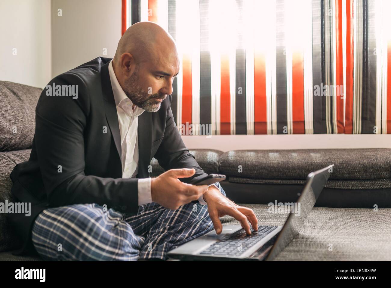 Konzept: Einengung durch Coronavirus, Covid-19. Mann Telearbeit im Wohnzimmer seines Hauses. In einem Executive-Anzug und Schlafanzug. Sitzen auf der Couch usi Stockfoto