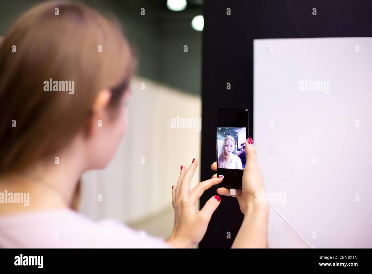 Eine junge Dame hält das Smartphone und schaut hinein wie im Spiegel, wenn sie Selfie macht. Weichstellung, Nahaufnahme, Rückansicht Stockfoto