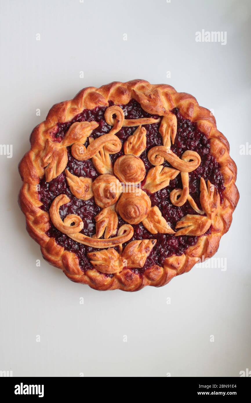 Köstlicher goldener runder Kuchen mit roter Kirsche und Lingonbeere, die mit Teigmuster auf weißem Hintergrund gefüllt sind. Stockfoto