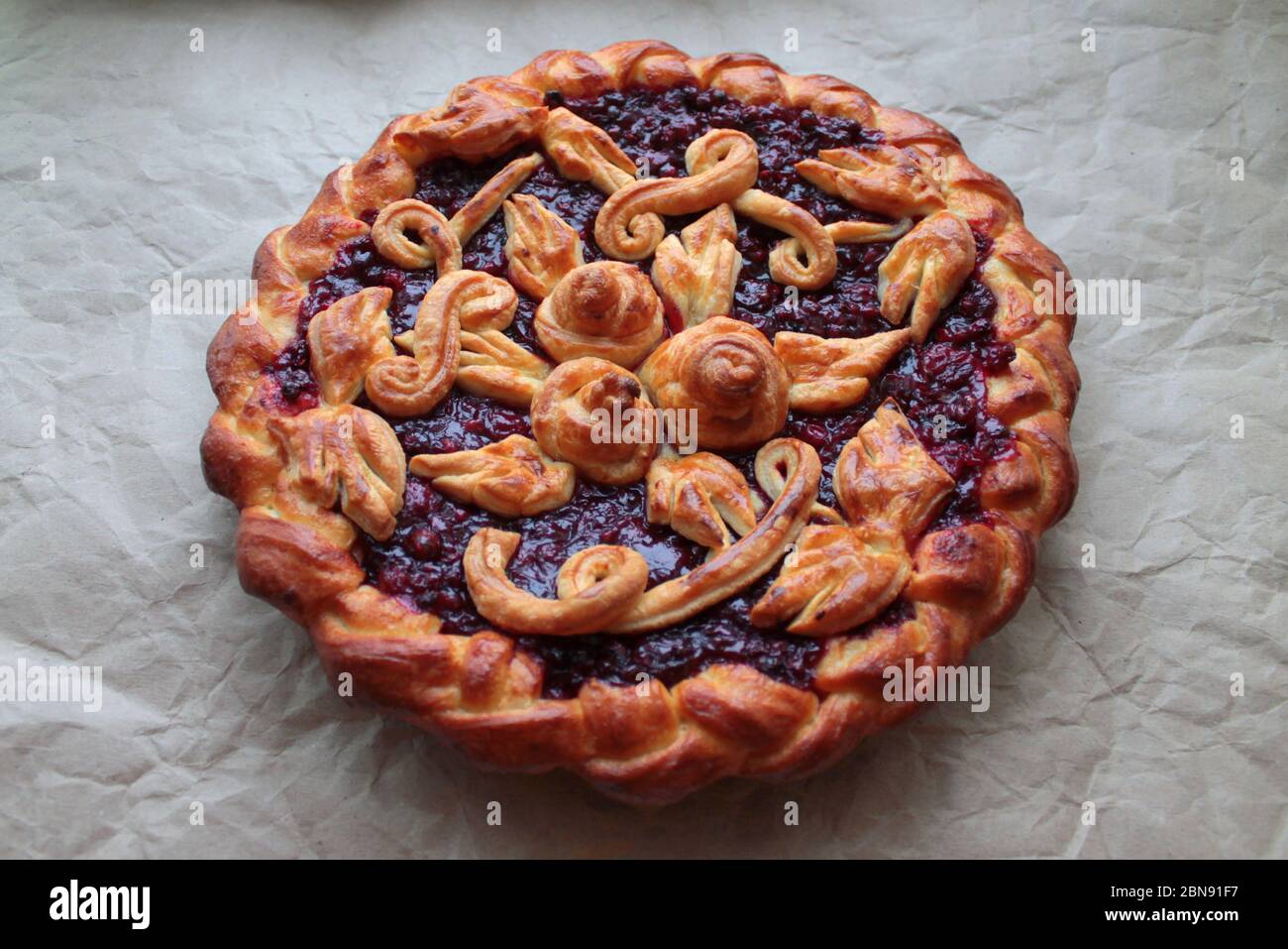 Köstlicher goldener runder Kuchen mit roter Kirsche und Lingonbeere, die mit Teigmuster auf zerknittertem Handwerkspapier gefüllt sind. Stockfoto