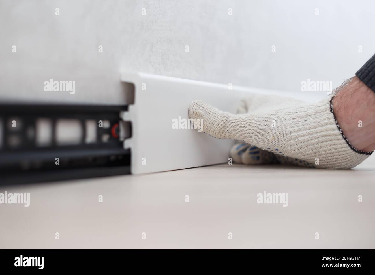 Mann, der neue Sockelleiste oder Bodenleiste an die Wand im Haus setzt. Stockfoto