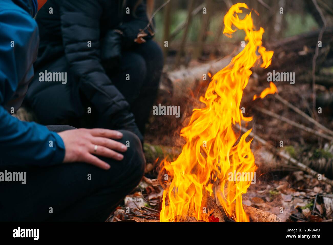 Der Mensch wärmt seine Hände auf Feuer. Brennendes Holz am Abend im Wald. Lagerfeuer im touristischen Camp in der Natur. Grillen und Kochen im Freien frische Luft Stockfoto